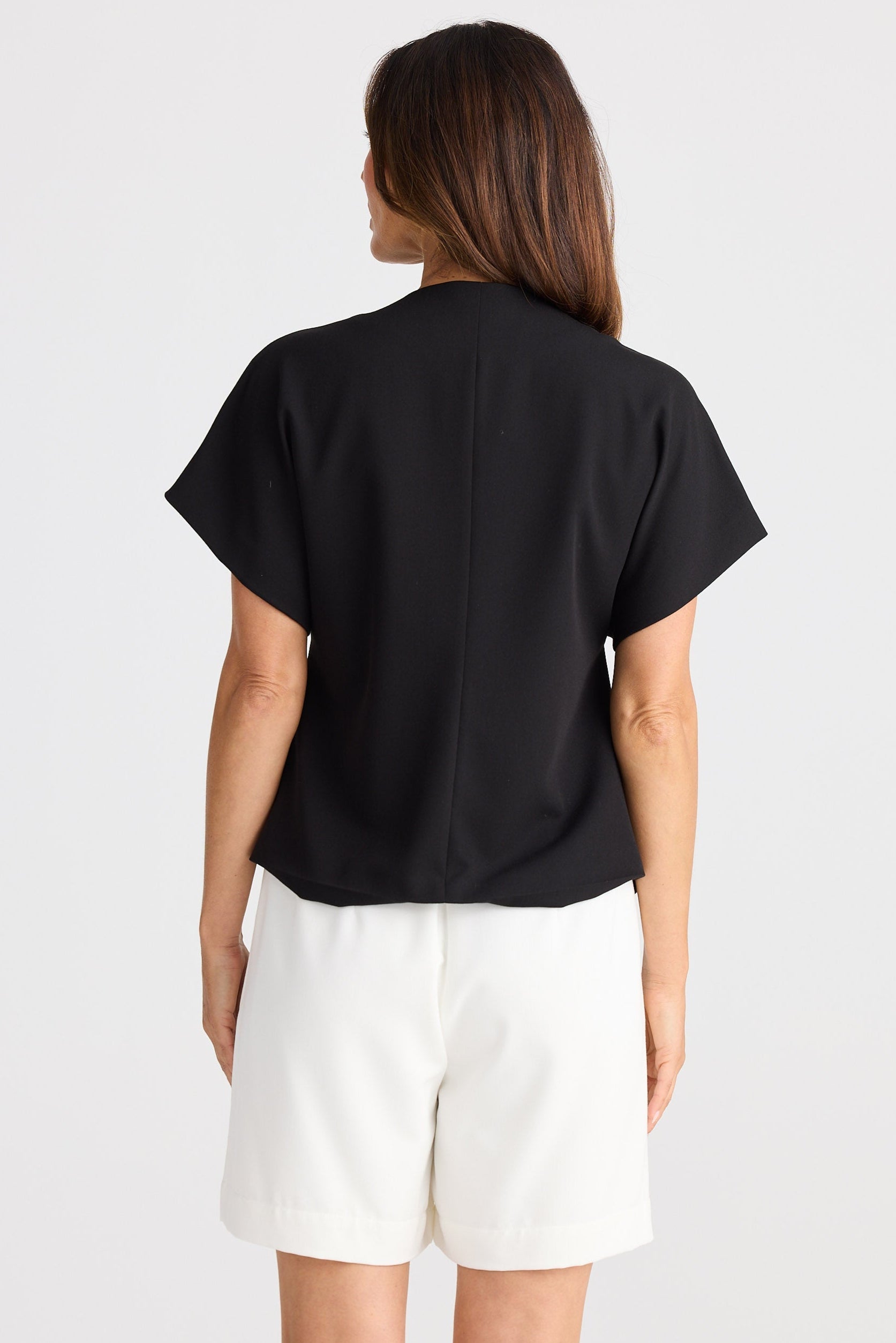 Person wearing a black t-shirt and white shorts on a plain background