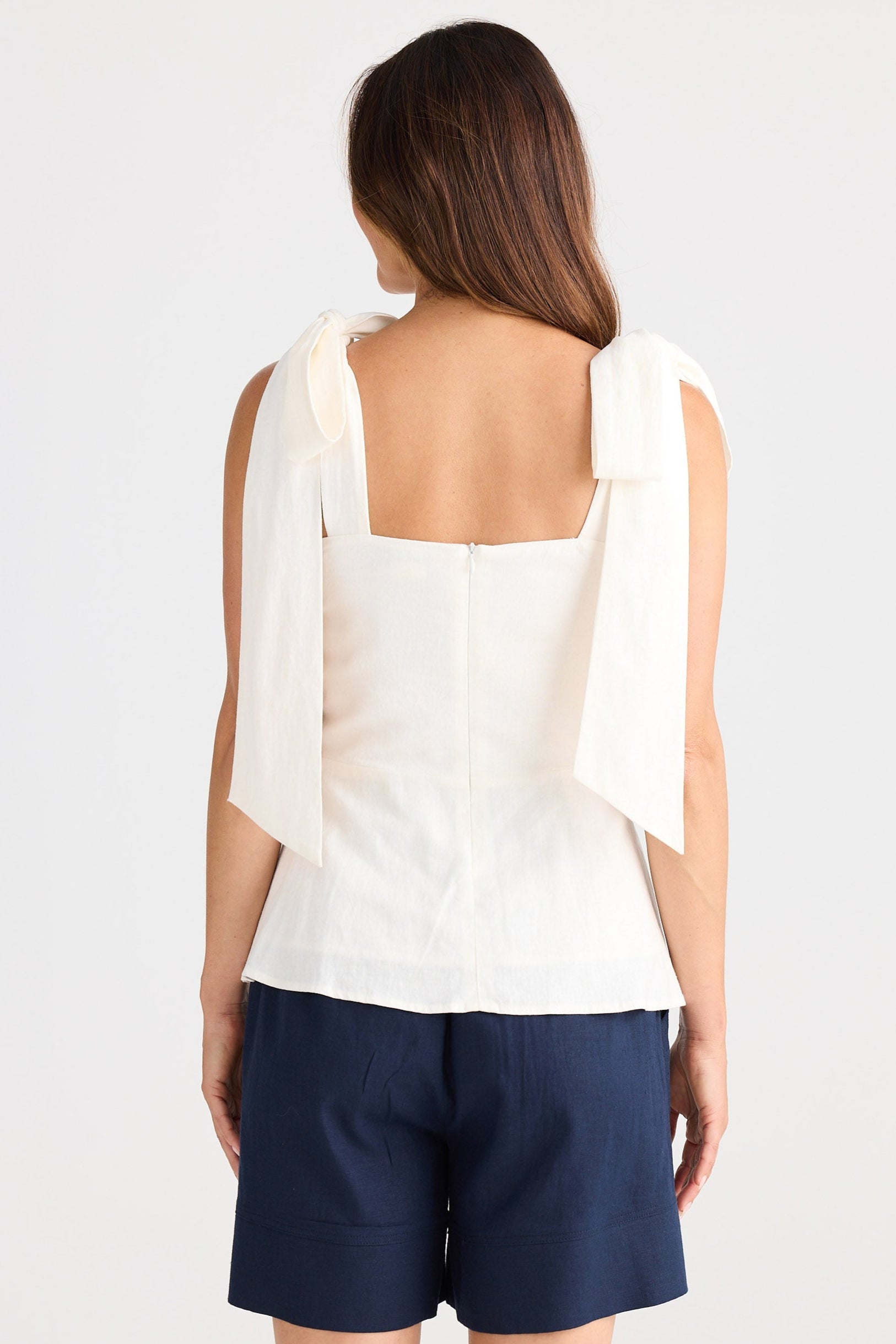 Woman wearing a white sleeveless top and navy shorts on a white background