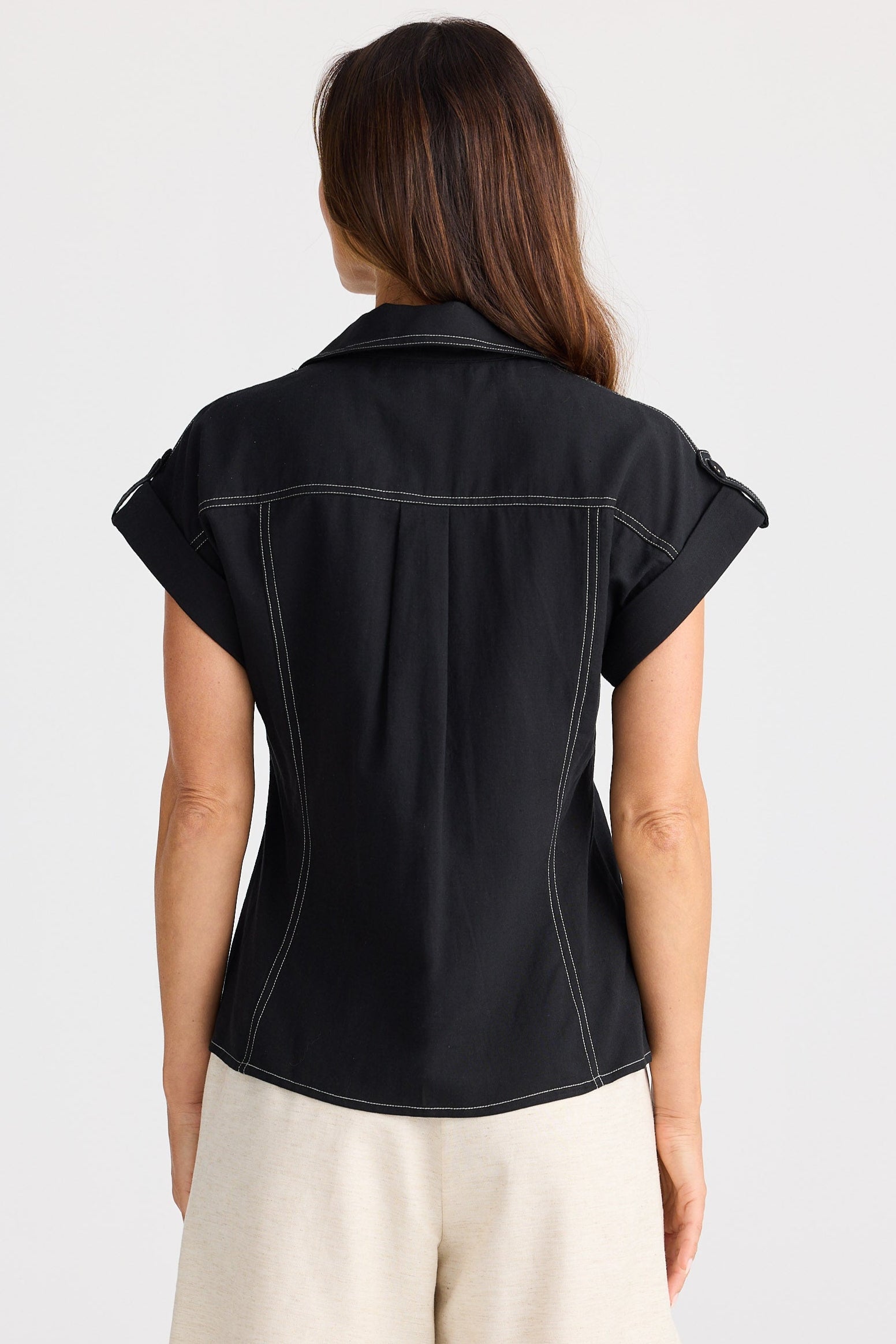 Woman wearing a black sleeveless shirt and beige shorts on a white background